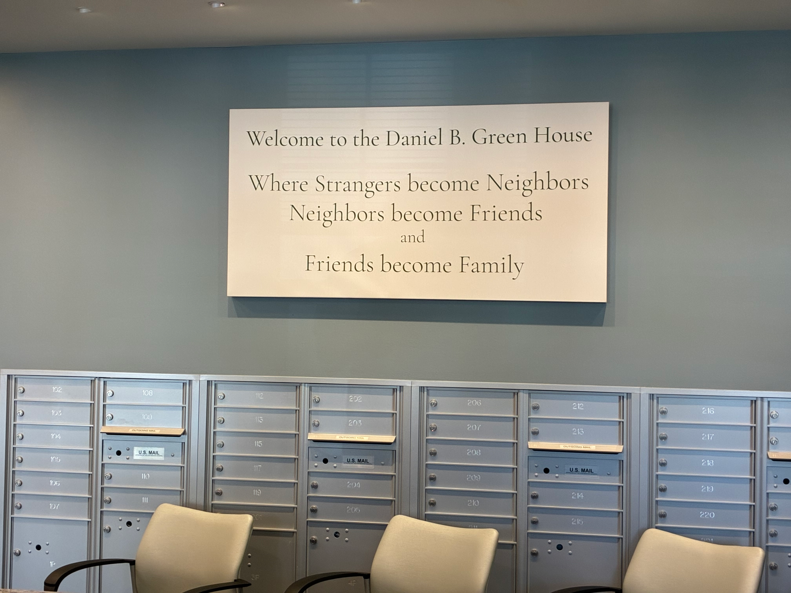 a plaque in the mailroom that says "welcome to the daniel b green house, where strangers become neighbors, neighbors become friends, and friends become family"